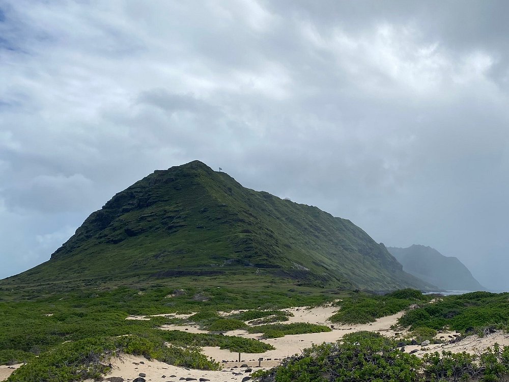 Kaʻena Point Trail with lush green mountain and cloudy sky.
