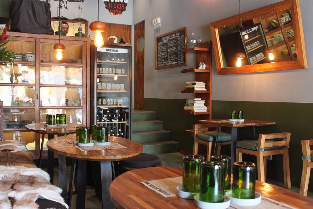 Cozy and earthy interior of Locavore To Go with round wooden tables and green glass decor.