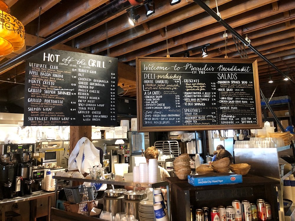 Counter view of Merridee's Breadbasket featuring a hanging chalkboard menu and deli items.