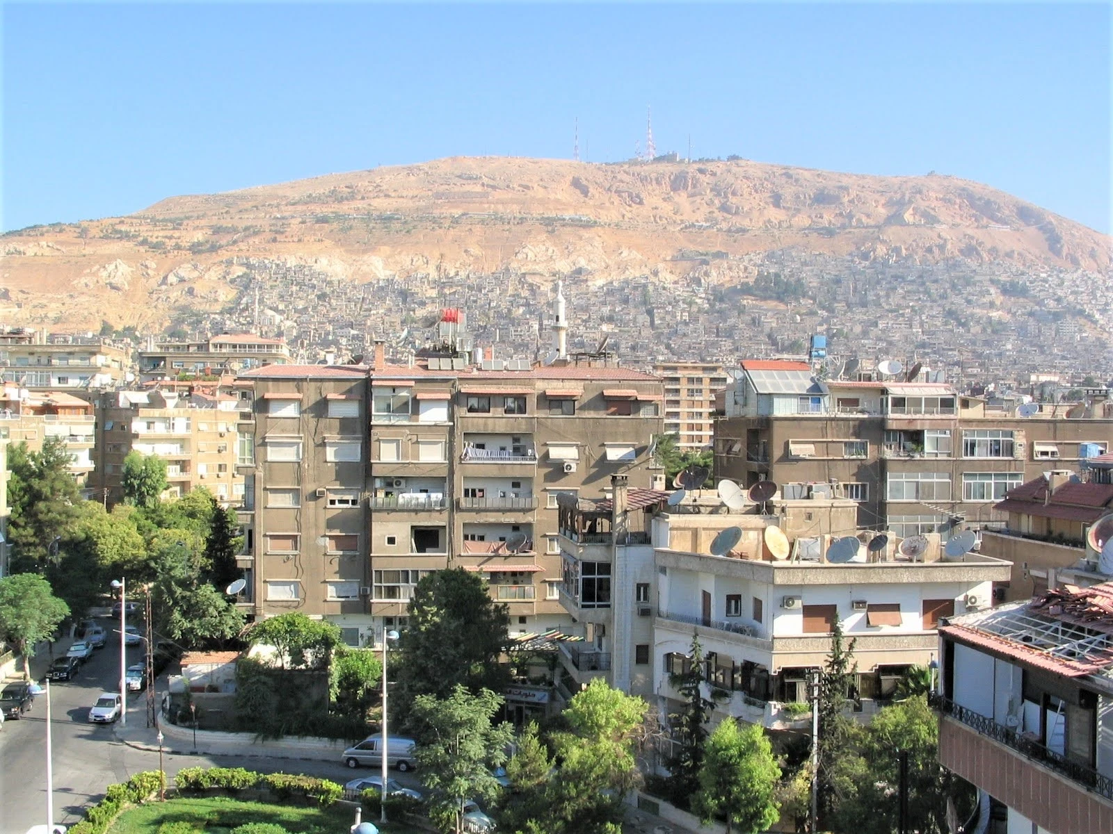 Mount Qasioun rising behind Damascus residential buildings with communication towers visible on the summit.