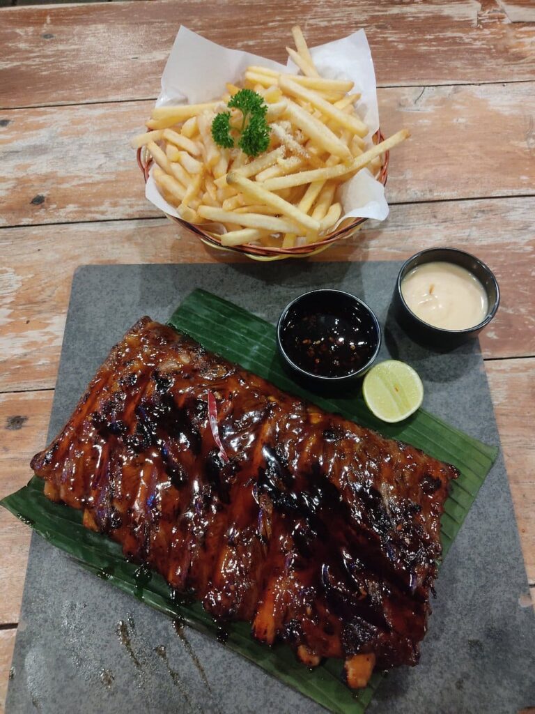 Sticky glazed ribs and fries served at Naughty Nuri’s Ubud on a rustic wooden table.