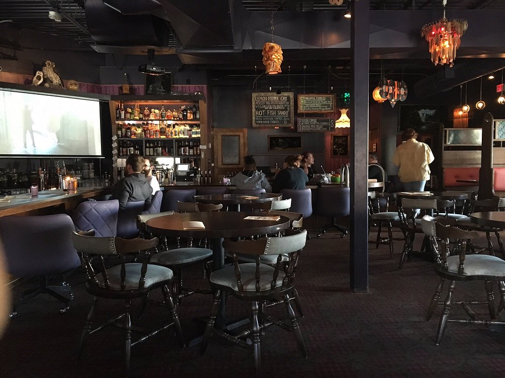 Dimly lit retro bar with purple chairs and a projector screen at Nite Owl.