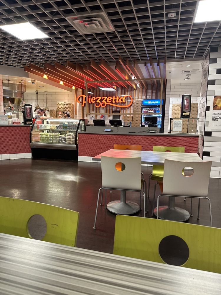 Modern counter-service setup at Piezzetta Pizza Kitchen with colorful chairs and a bright neon sign.