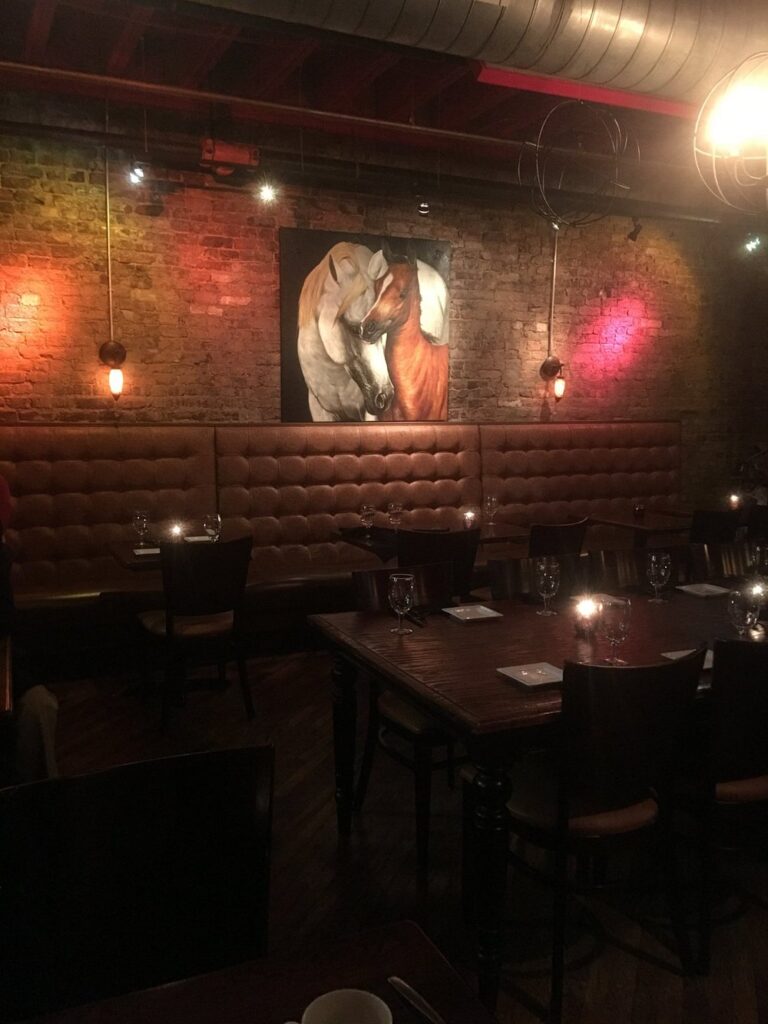 Dimly lit dining room at Red Pony with leather booths, brick walls, and candlelit tables.