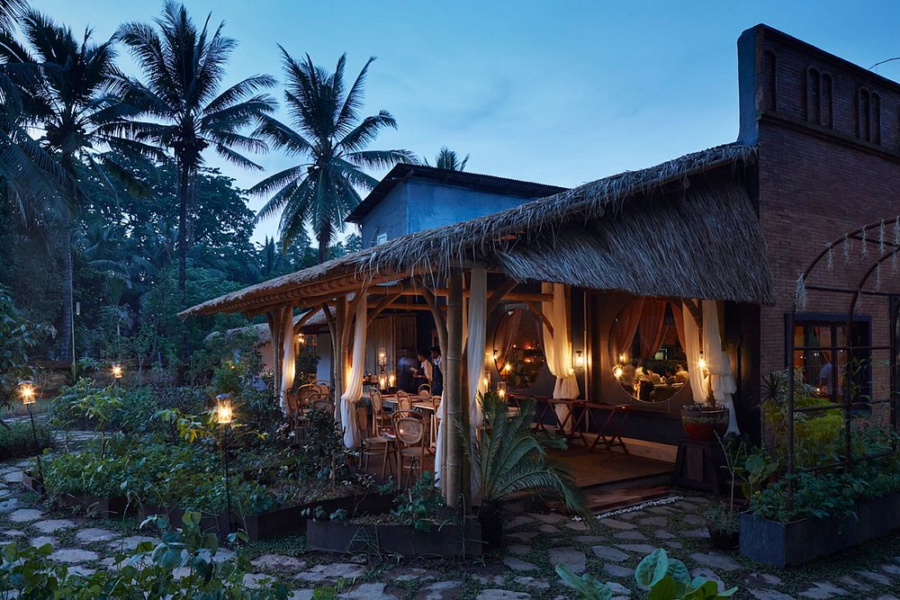 Romantic thatched-roof setting at Room 4 Dessert surrounded by lush greenery and candlelight.
