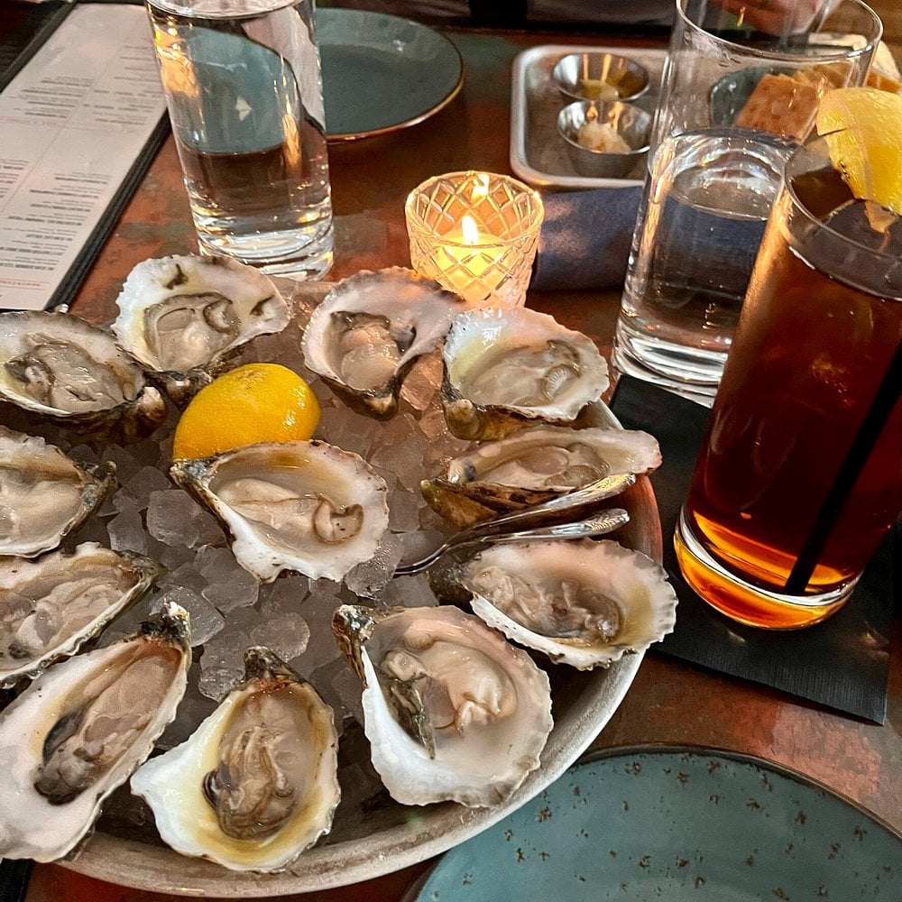 A chilled platter of oysters at St. Roch Fine Oysters + Bar, served on ice with lemon, drinks, and candlelight.