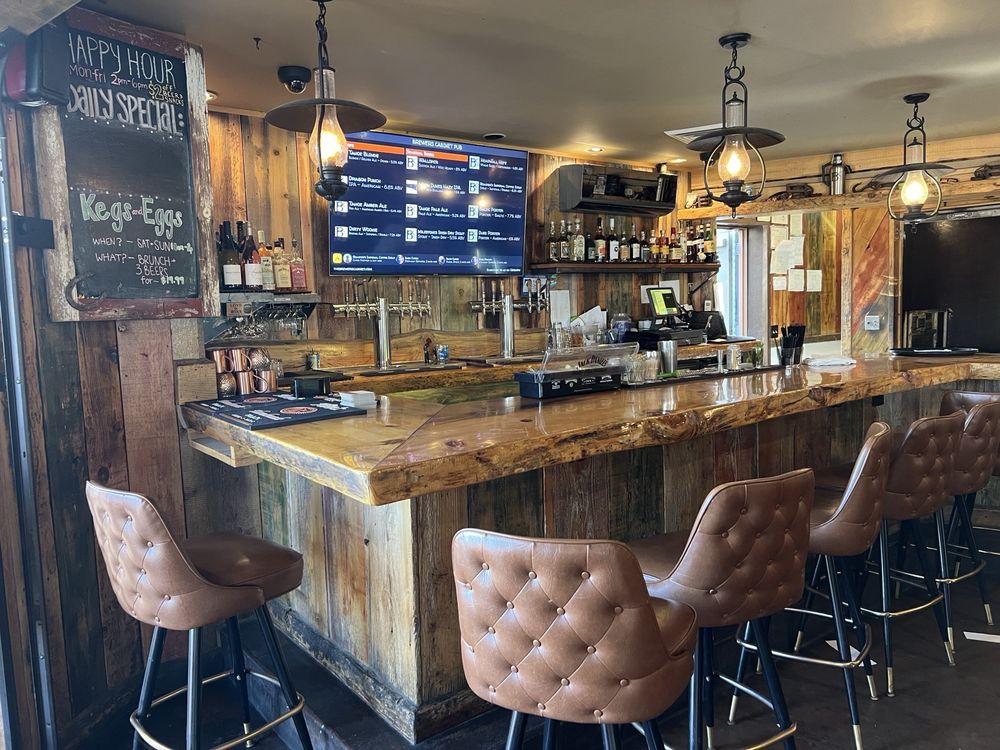 Wood-accented bar area at The Brewer’s Cabinet with leather stools and a beer tap list on screen.