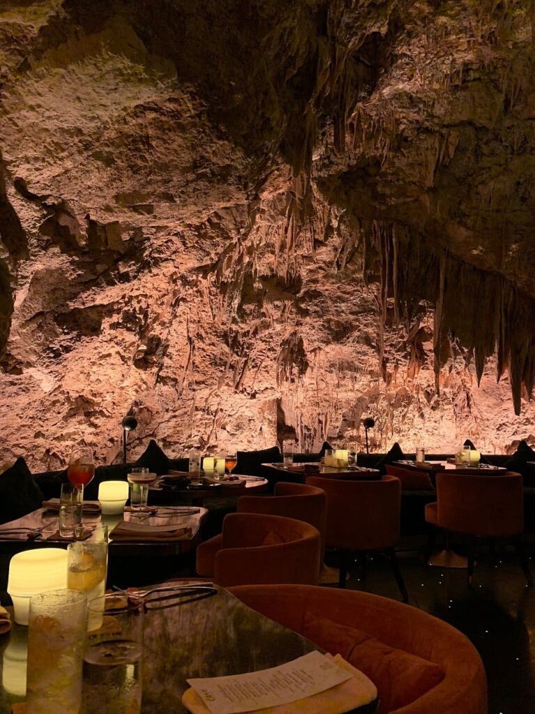 Dramatic dining experience inside The Cave Bali with natural rock walls and glowing table lights.