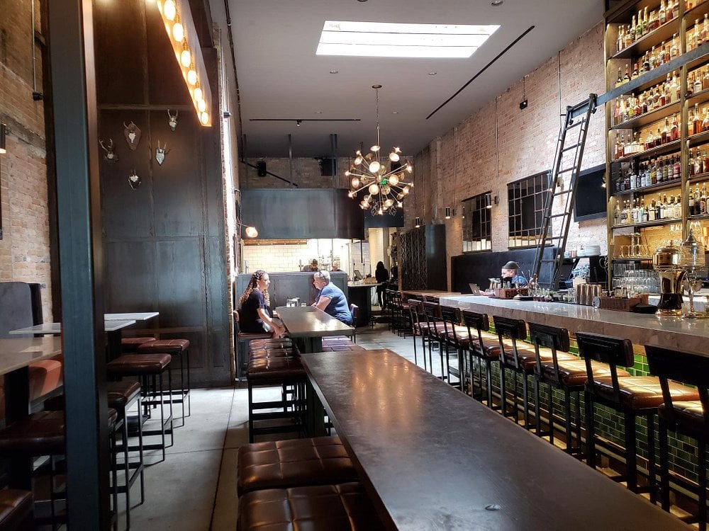Industrial-style bar with exposed brick and tall shelves at White Horse Spirits & Kitchen.