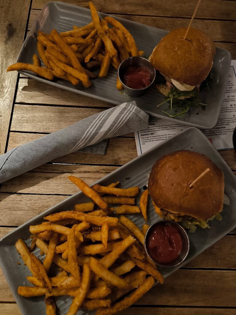 Two burger and fries plates at Wye Hill Kitchen & Brewing, served with ketchup on rustic wooden tables.