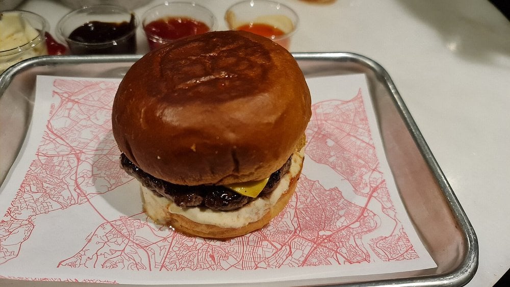Close-up of a burger on a tray at Zula with sauces in the background.