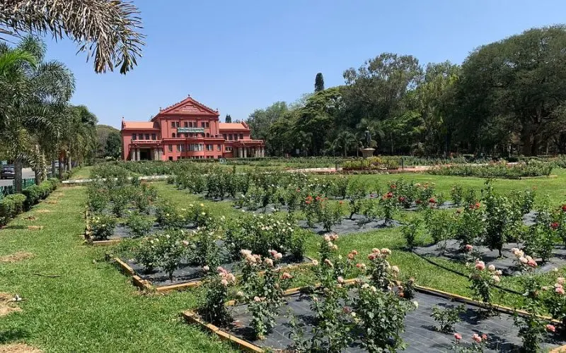 Bengaluru with a large red building surrounded by gardens and flower beds.