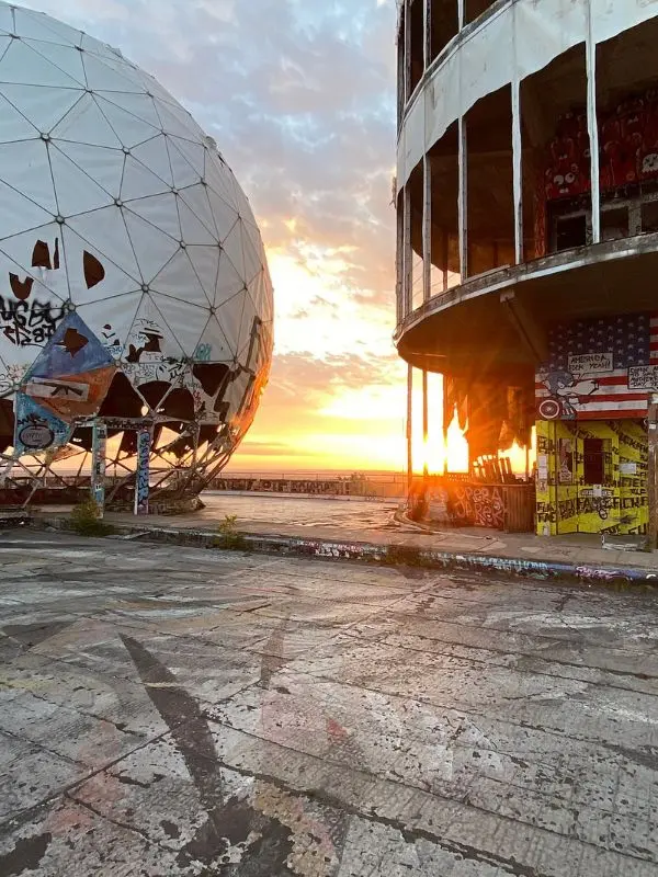 Graffiti covers the abandoned radar domes at Teufelsberg during sunset.