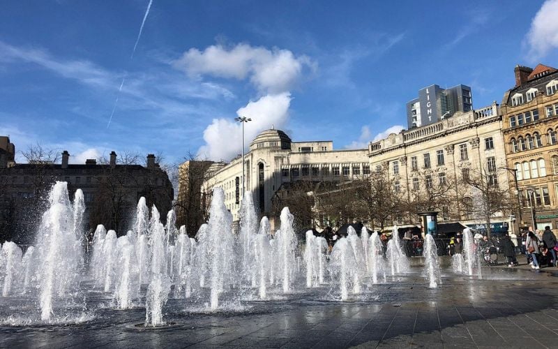 A lively fountain square surrounded by historic buildings in Manchester.