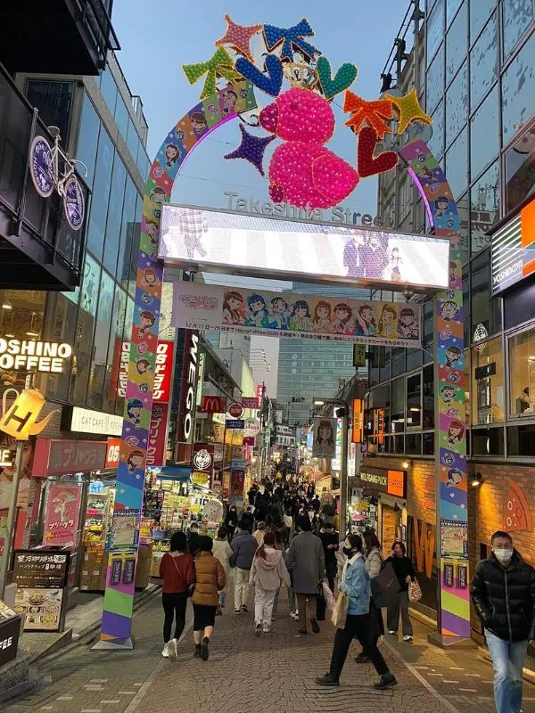 Crowds walking under the entrance arch of Takeshita Street in Harajuku.