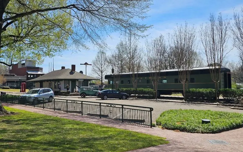 Collierville train depot area with a vintage railcar and parked cars.