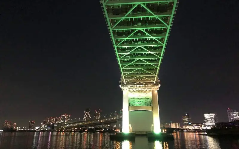 Night view of the Rainbow Bridge illuminated in green over the water.