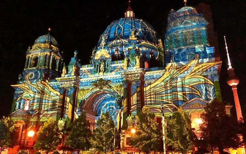 The Berliner Dom is illuminated with colorful projections at night.
