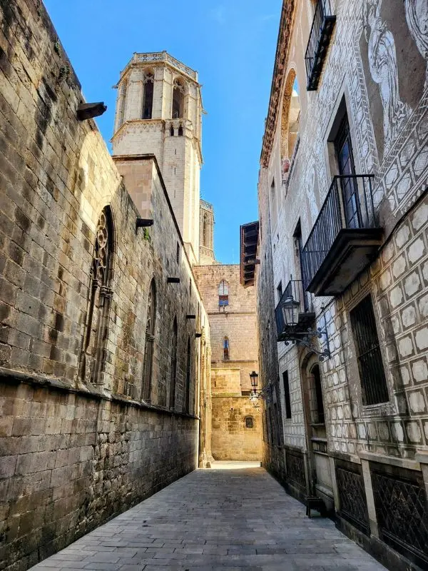 Narrow stone street with church tower in Barcelona.
