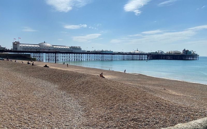 Brighton Pier stretching out over the calm sea with a pebbled beach in the foreground.