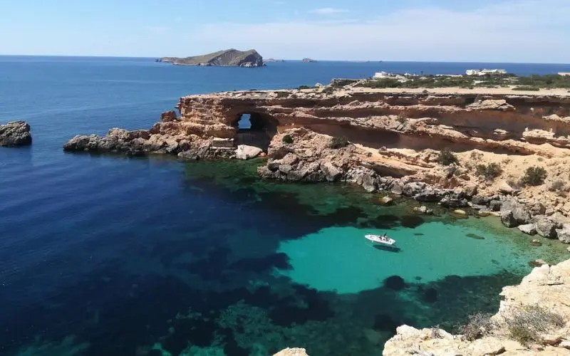 A rocky coastline with turquoise waters and a sea cave in Ibiza, Spain.