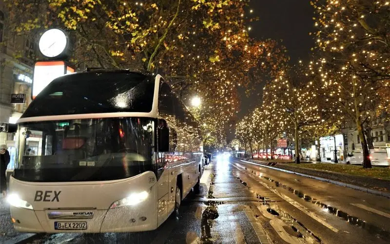 A BEX sightseeing bus is parked on a Berlin street lined with holiday lights.