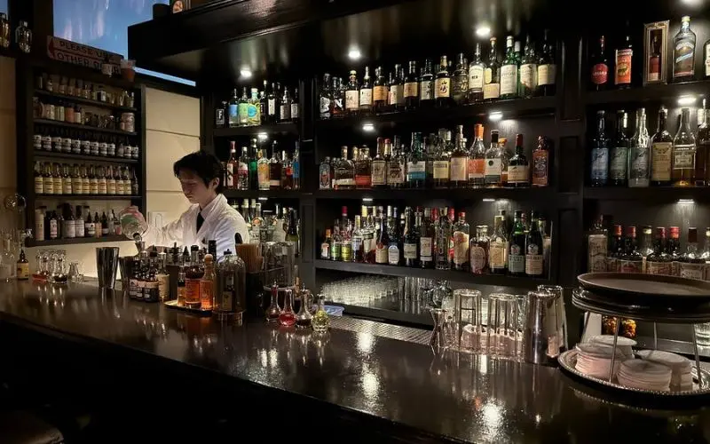 A bartender prepares drinks at Bar Trench surrounded by bottles.
