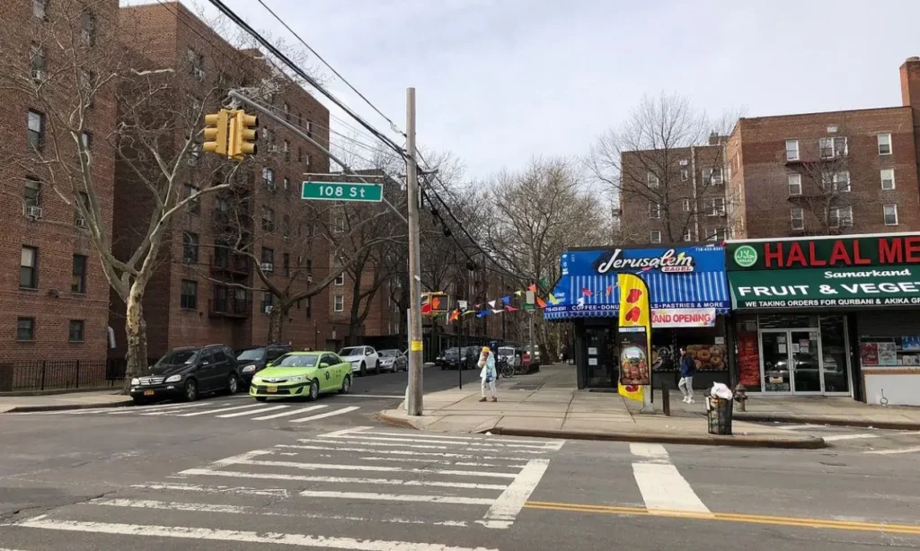 A street corner in Forest Hills with shops, cars, and a 108 St street sign.