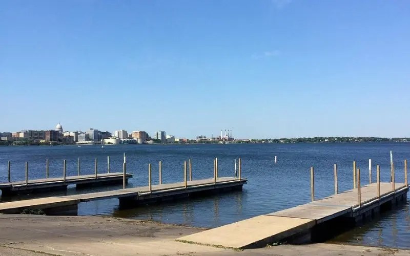 Wooden docks extending into the water with a view of Maple Bluff across the lake.