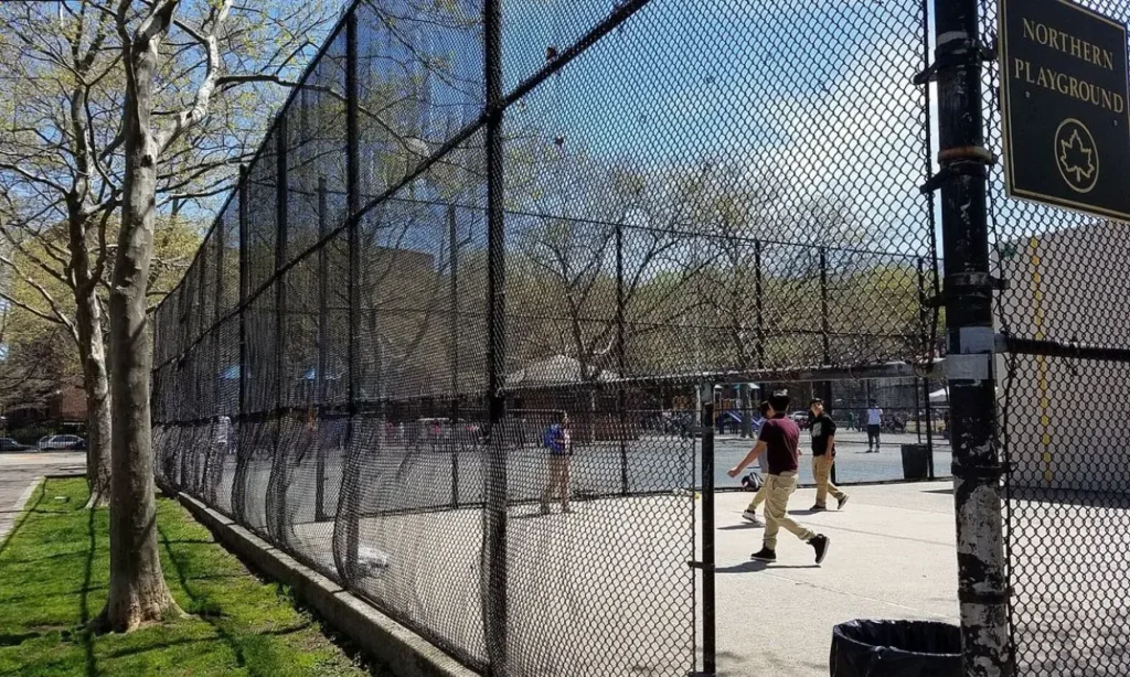 A fenced playground with people playing handball at Northern Playground in Jackson Heights.