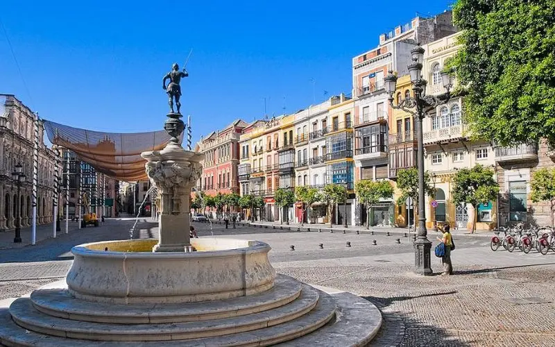 Fountain in a sunny square surrounded by colorful buildings in Seville.
