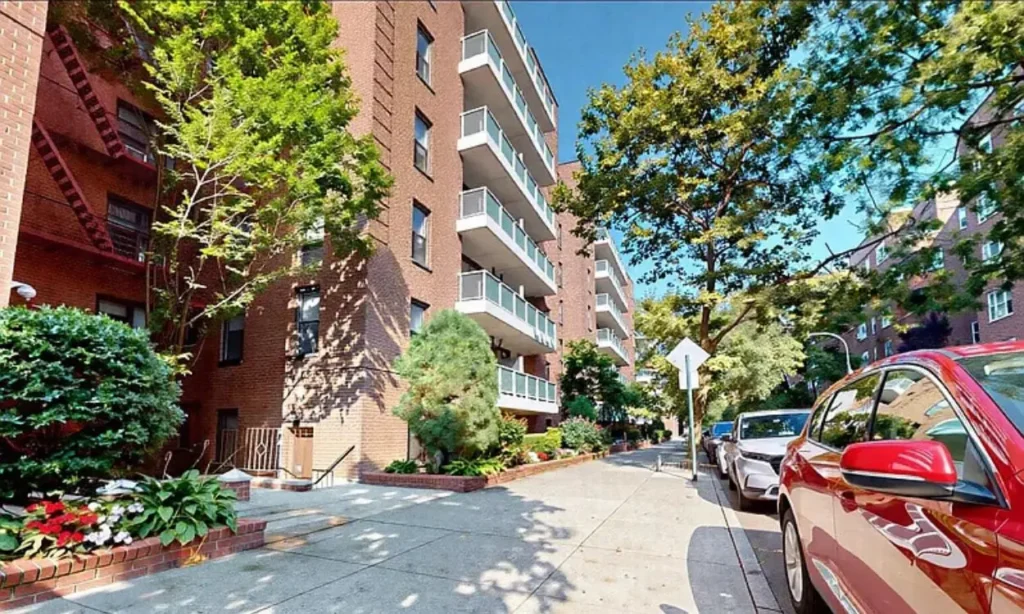A tree-lined sidewalk beside brick apartment buildings in Kew Gardens.