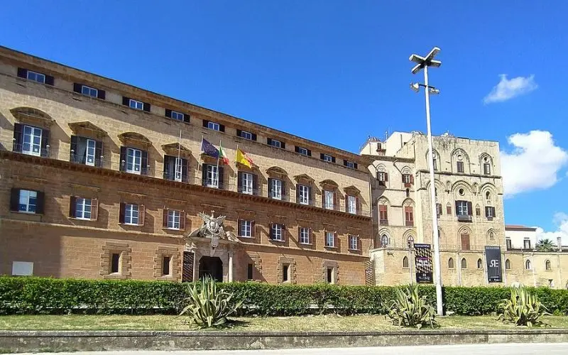 Large historic stone building with flags in Palermo.
