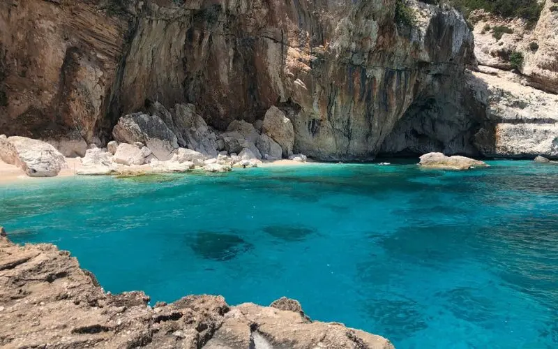 Clear turquoise waters lap against rocky cliffs in Sardinia.