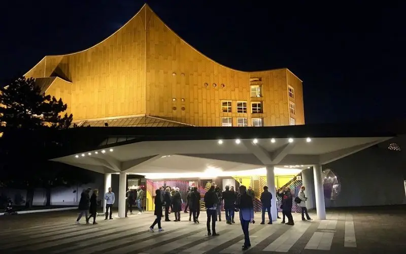 Visitors gather outside the Berlin Philharmoniker concert hall at night.