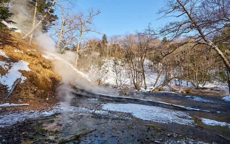 Steam rises from a hot spring surrounded by snow and trees in Hokkaido.
