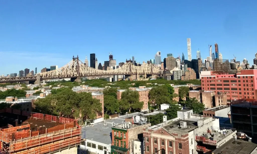 A cityscape view of Long Island City with the Queensboro Bridge and Manhattan skyline in the background.