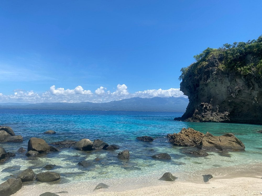 Clear blue water and rocky shoreline at Apo Island with mountains in the distance.