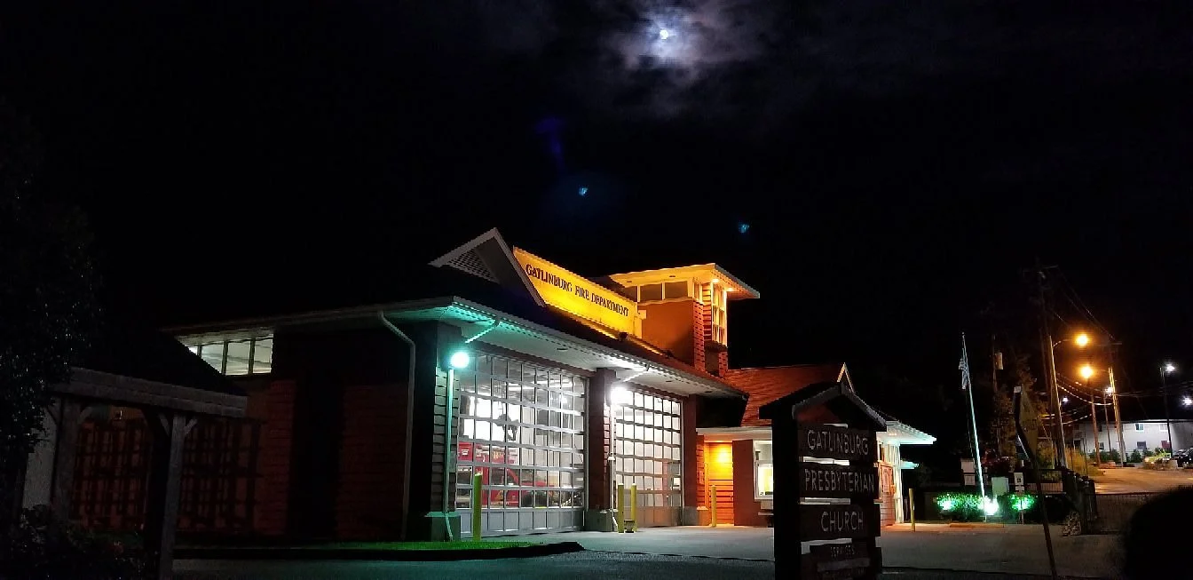 Gatlinburg churches illuminated at night under full moon with dark cloudy sky.