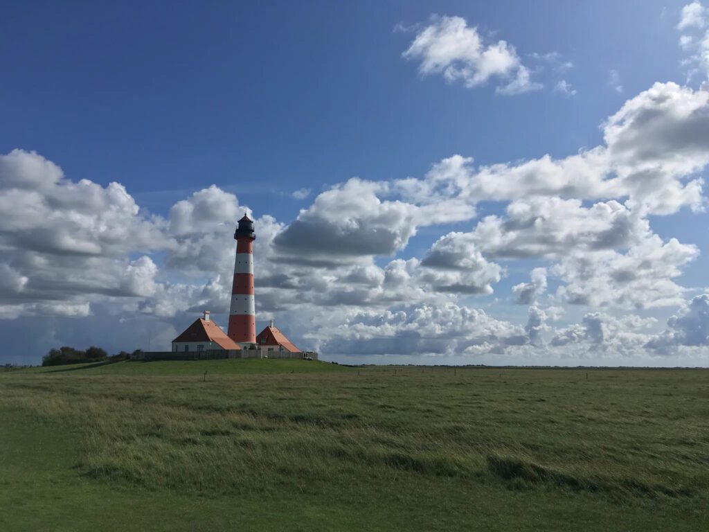 A red and white lighthouse stands in Schleswig-Holstein Wadden Sea National Park under a partly cloudy sky.