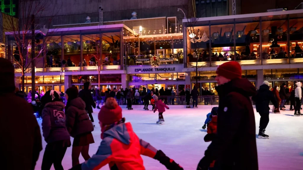 Skaters on the illuminated outdoor ice rink at Esplanade Tranquille at night