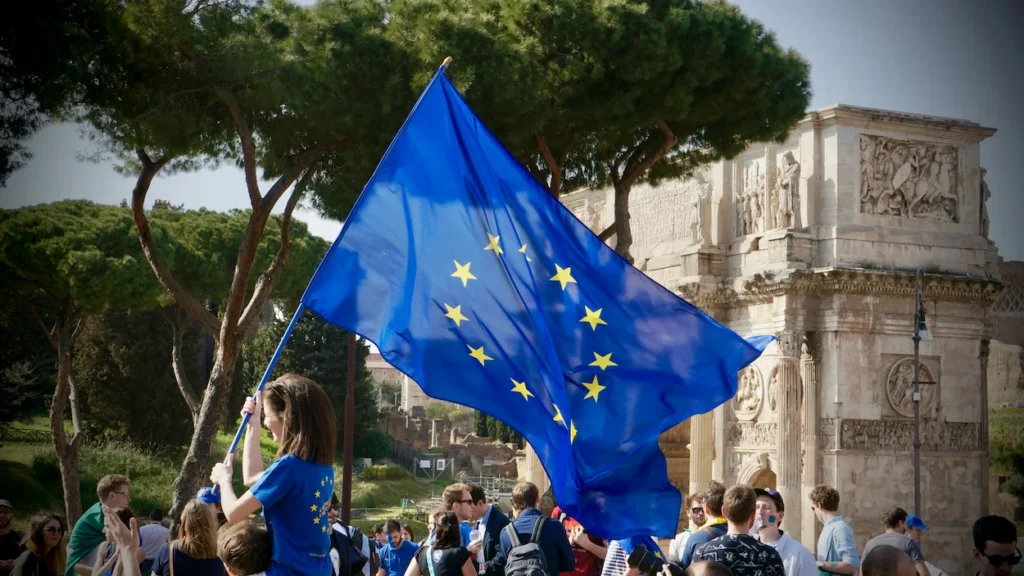 A person waving an EU flag in front of the Arch of Constantine
