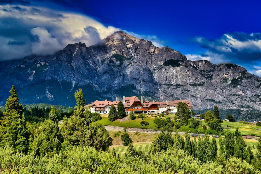 Llao Llao Hotel nestled on a green hill beneath a massive rugged mountain peak