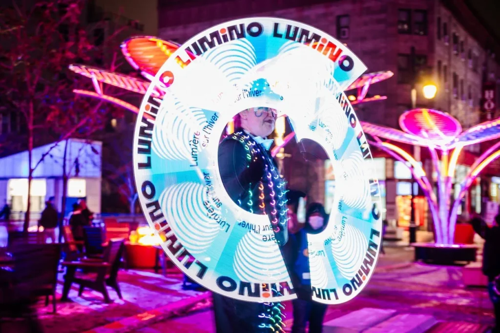 A street performer spinning a glowing LED hoop displaying the word Lumino at night