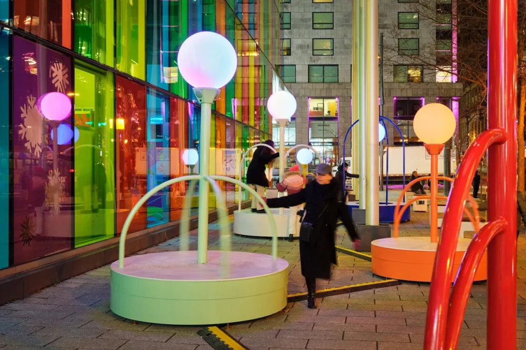People spinning on glowing light installations outside a colorful building
