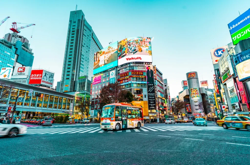 A bus driving through the wide Shibuya Crossing intersection surrounded by skyscrapers
