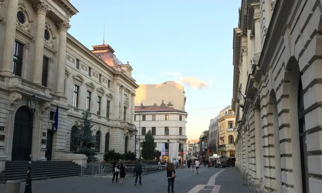 A street in Romania lined with grand historic buildings and people walking.