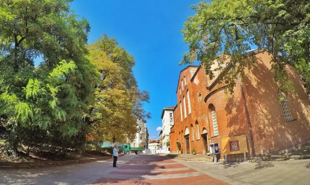 A brick church and trees under a bright blue sky in Bulgaria.
