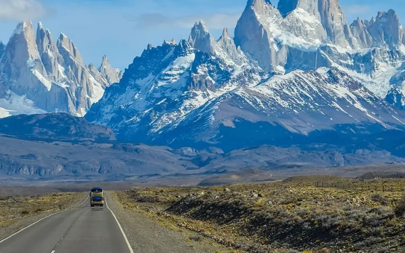 Chile has snowy peaks of Patagonia rising behind a long road.