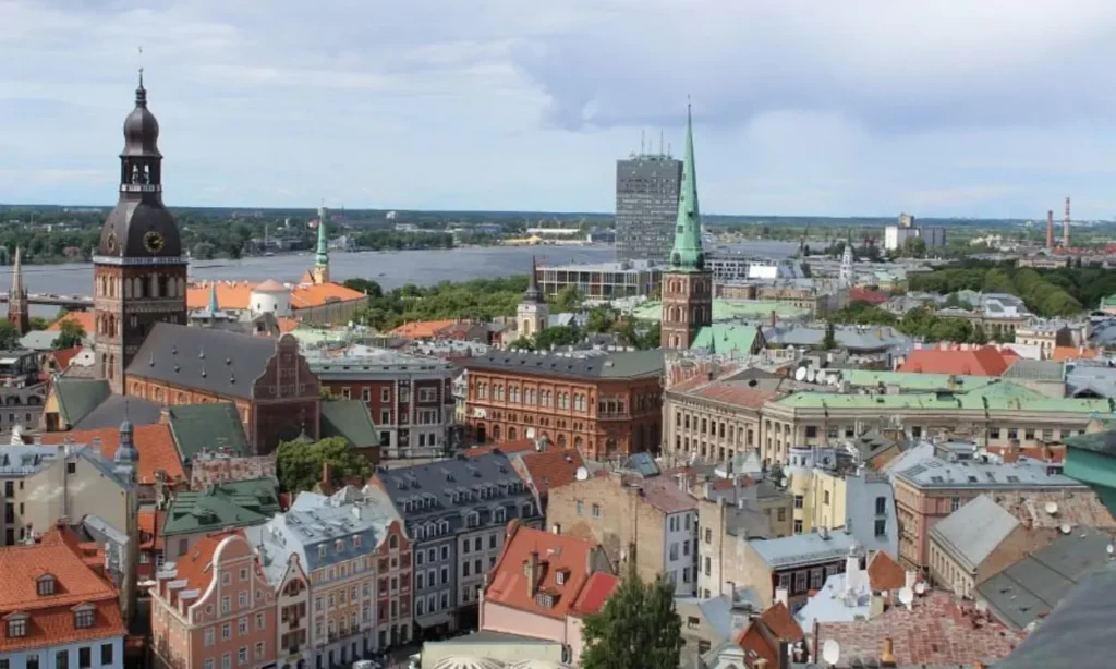 A cityscape of Latvia with church towers, red roofs, and a river in the background.